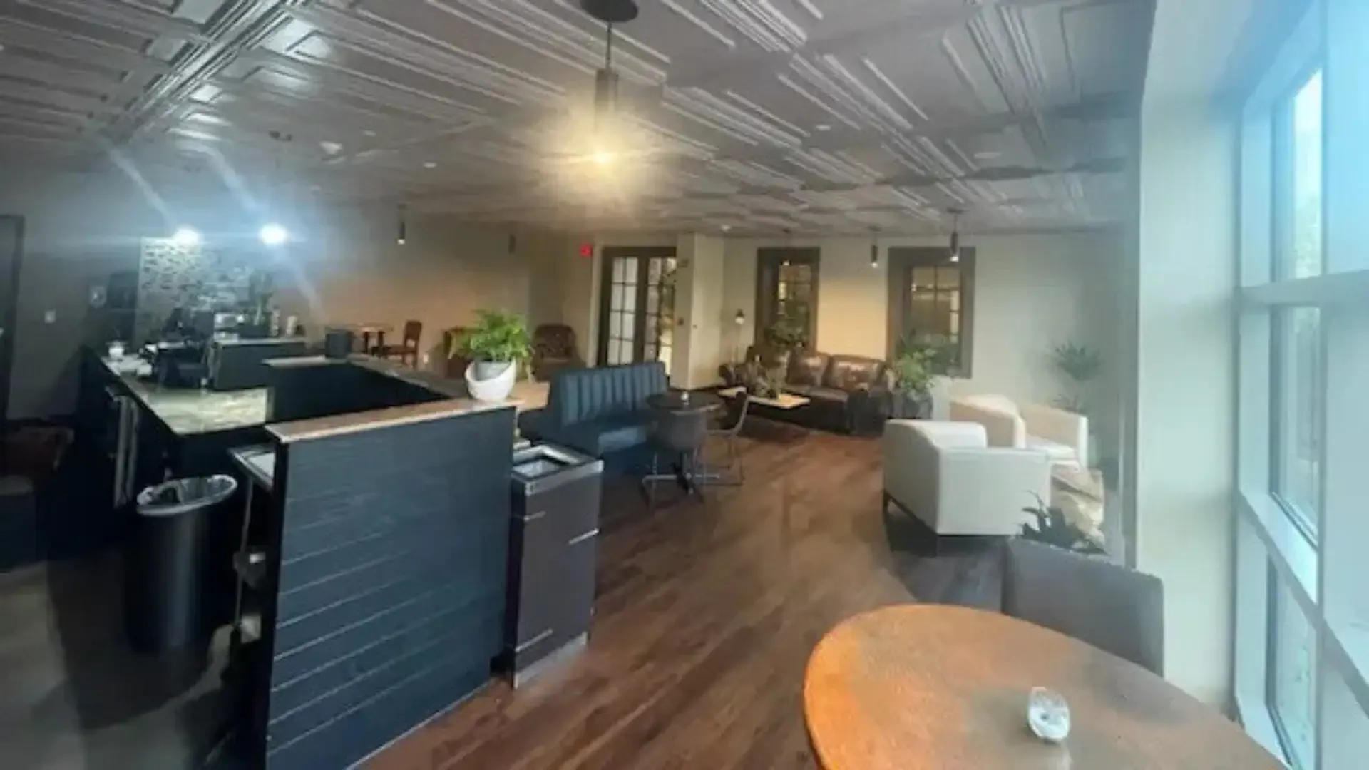 Open-plan office lounge lit by pendant and recessed fixtures under a pressed-tin ceiling